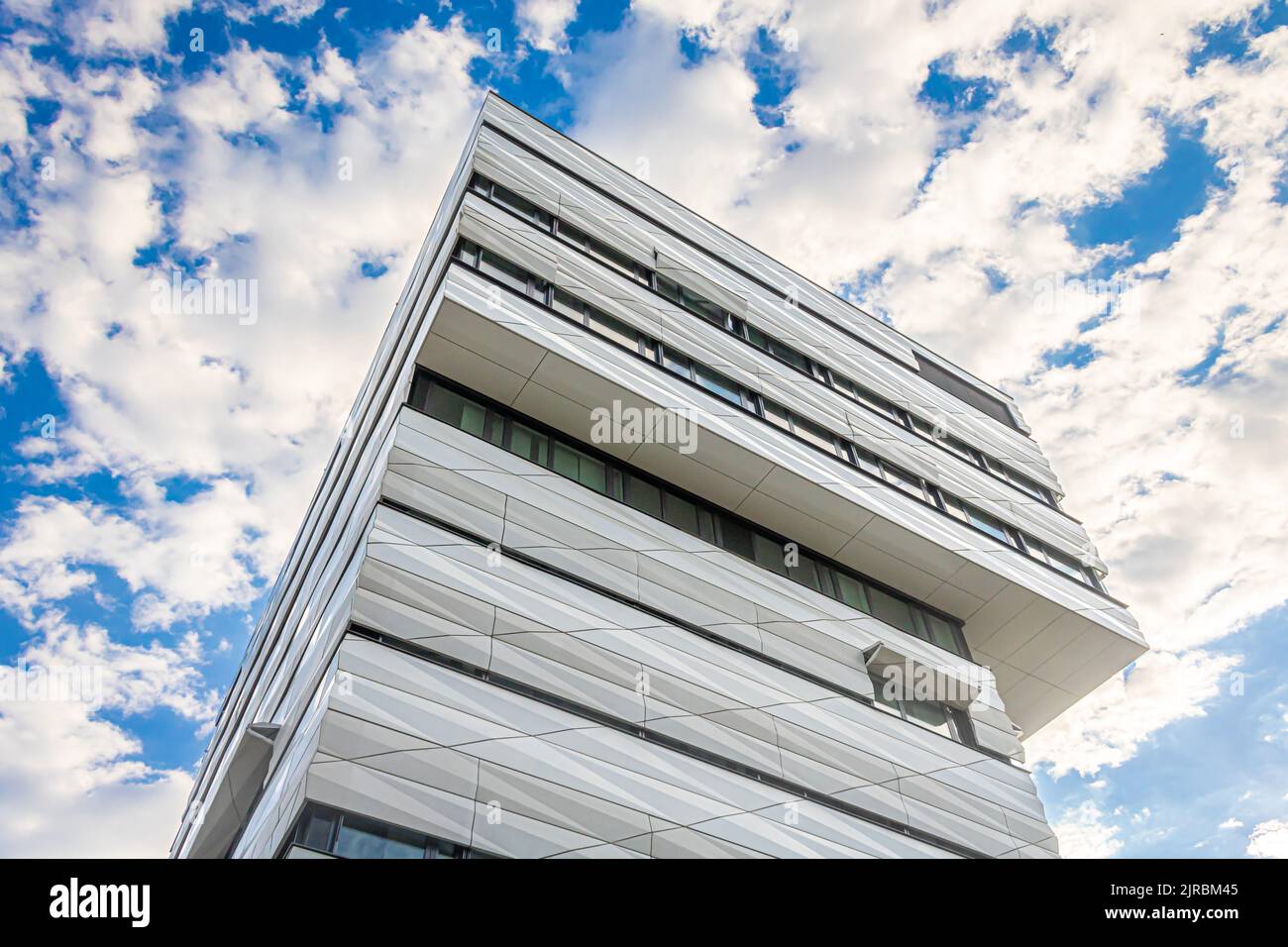 a perspective view of modern building with overhanging upper floors and striking facade against a dramatically lit sky with partial cloud cover Stock Photo