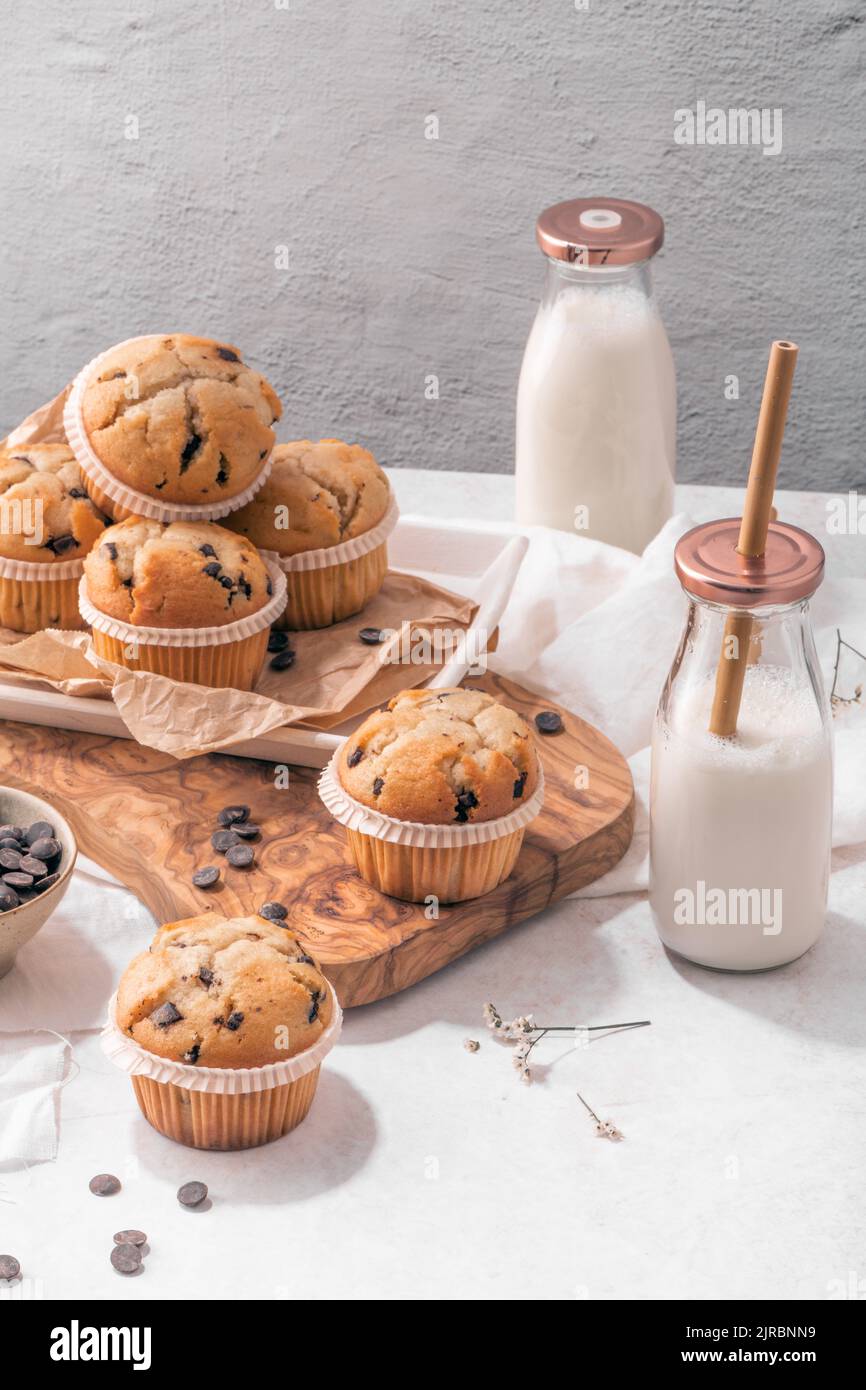 Chocolate chip muffins with milk served on glass bottles on white kitchen countertop Stock Photo