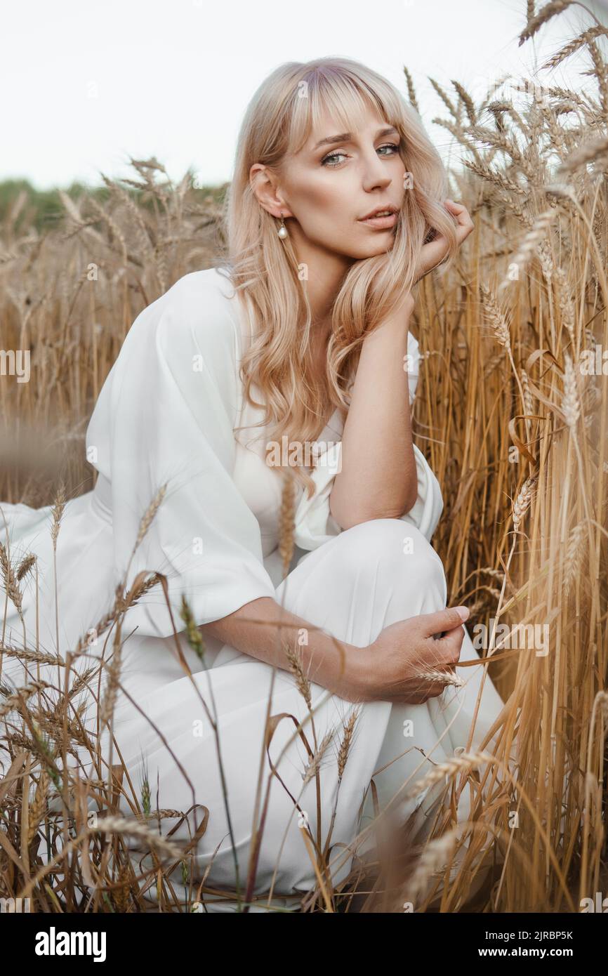A blonde woman in a long white dress walks in a wheat field. The ...