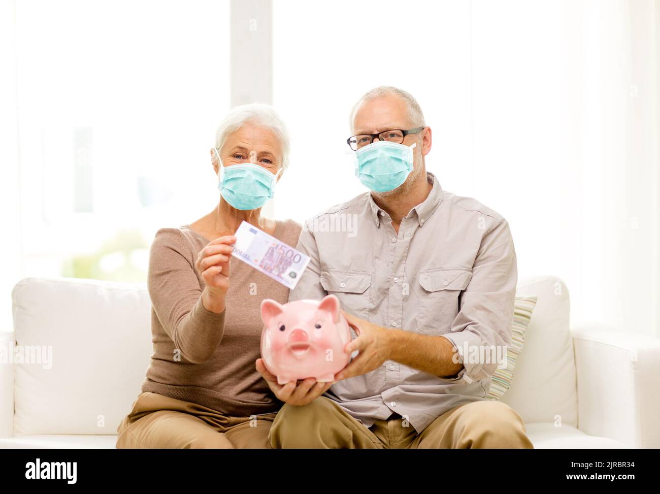 old couple in masks putting money into piggy bank Stock Photo - Alamy