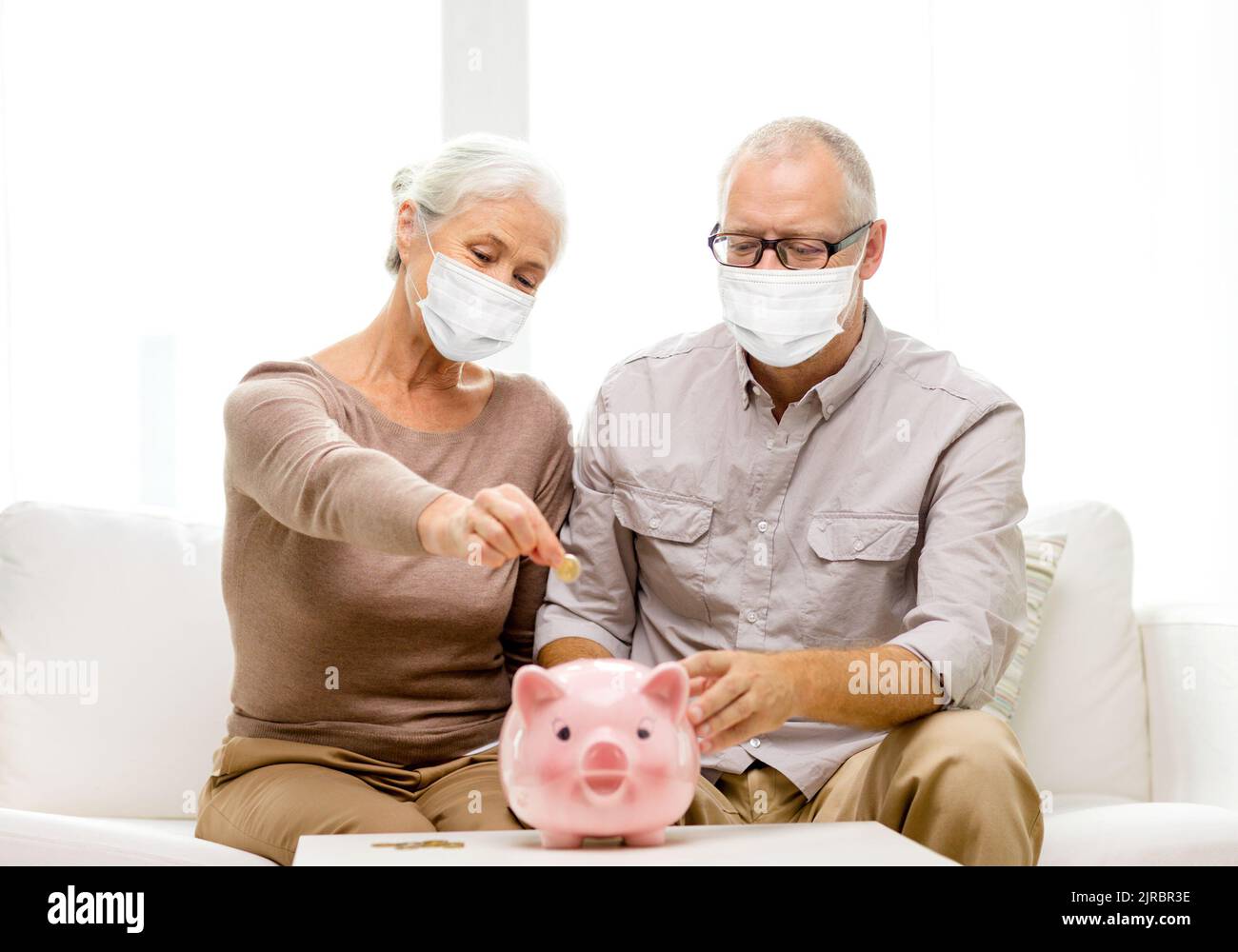 old couple in masks putting coin into piggy bank Stock Photo - Alamy