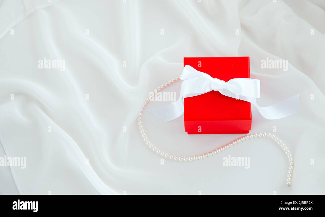 Red gift box with white ribbon on white silk background Stock Photo - Alamy