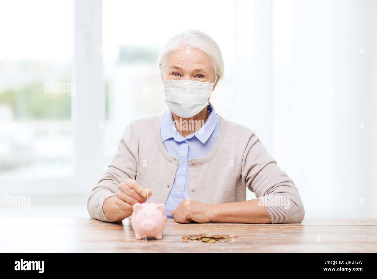 old woman in mask putting coin into piggy bank Stock Photo - Alamy