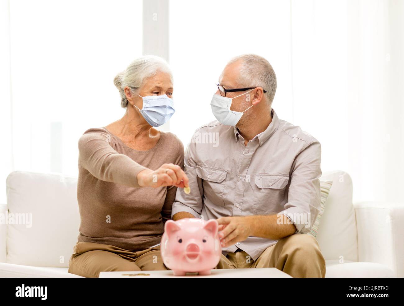 old couple in masks putting coin into piggy bank Stock Photo - Alamy