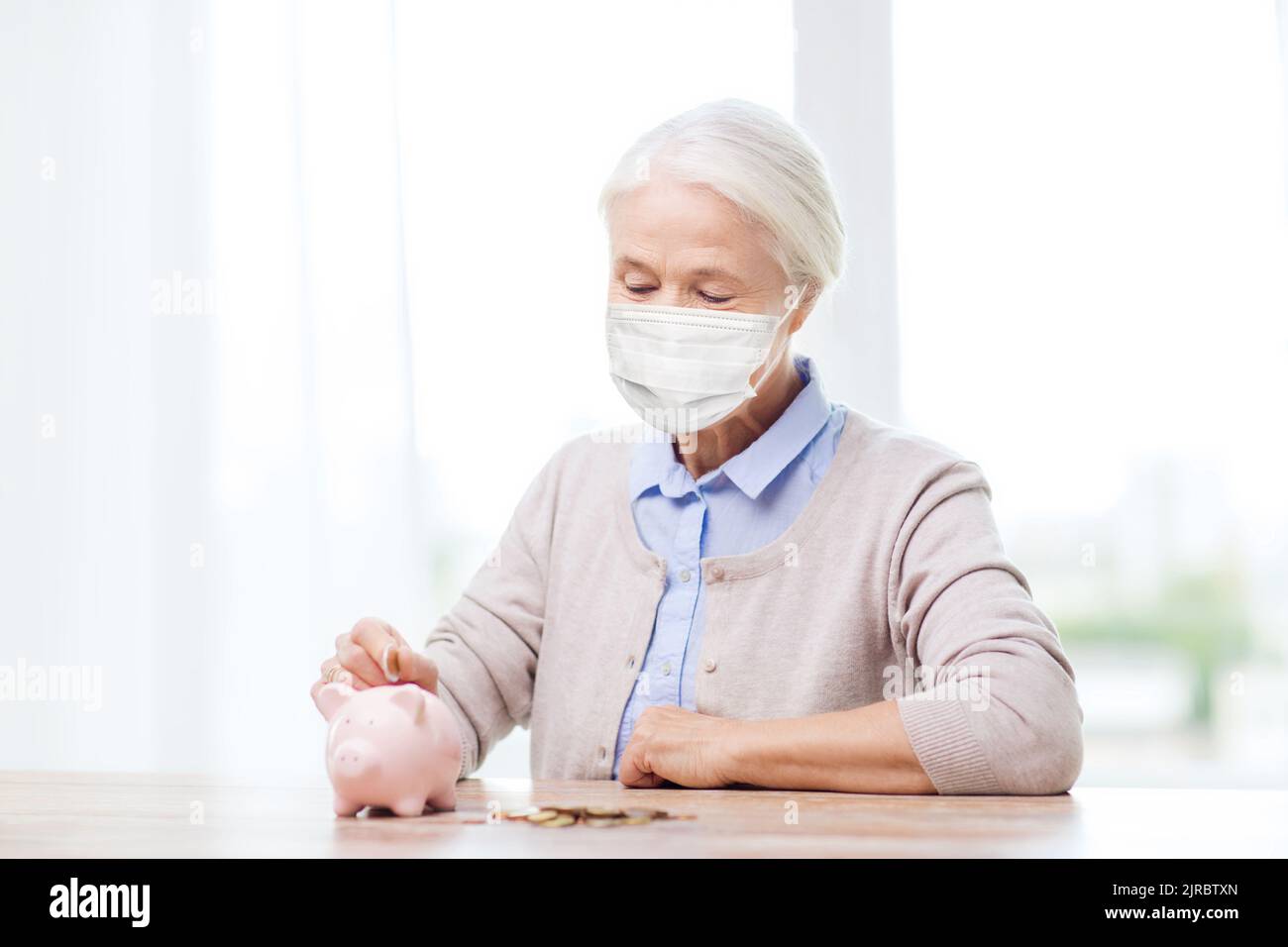 old woman in mask putting coin into piggy bank Stock Photo - Alamy