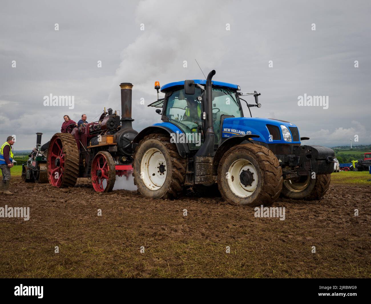 Modern tractor towing a vintage traction engine and steamroller out of the mud at the Launceston Steam & Vintage Rally, Cornwall, UK Stock Photo