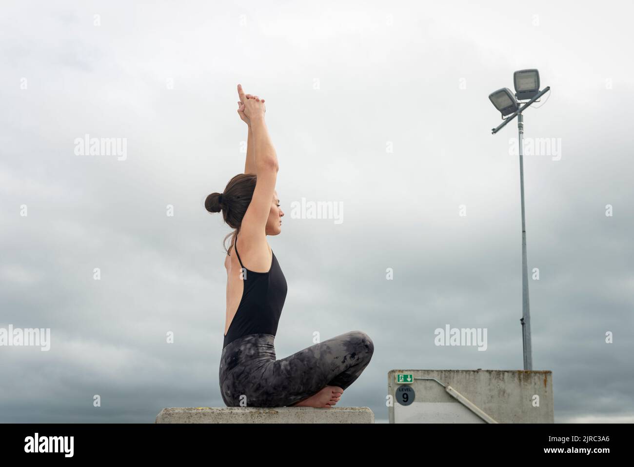 Young fitness woman meditating in lotus position sitting, urban background. Sporty girl doing yoga. Stock Photo