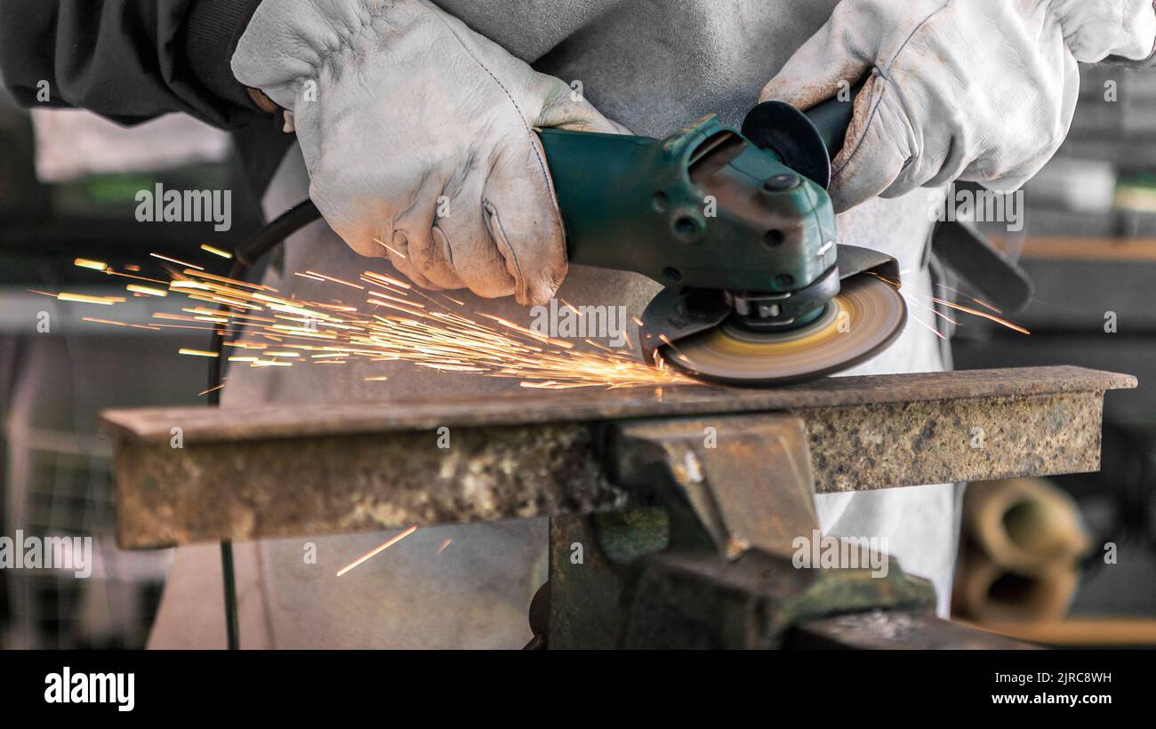 Craftsman grinding metal with disk grinder in workshop. Worker cleaning the steel seam. Cutting grinding wheel cut a piece of iron with sparks fly in Stock Photo