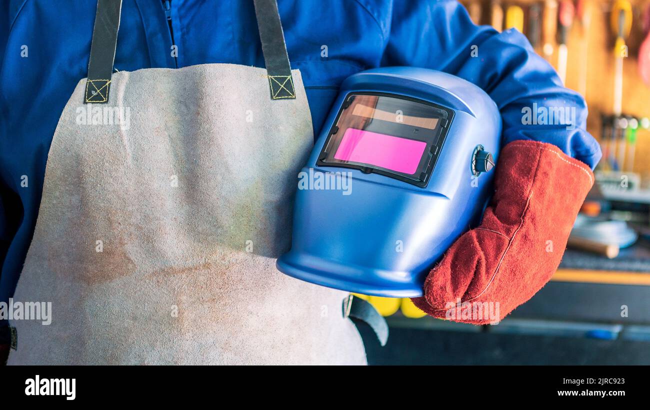 Locksmith in special clothes, helmet and gloves to works in production metalworking. Metal processing with a man using welding machine for steel seam. Stock Photo