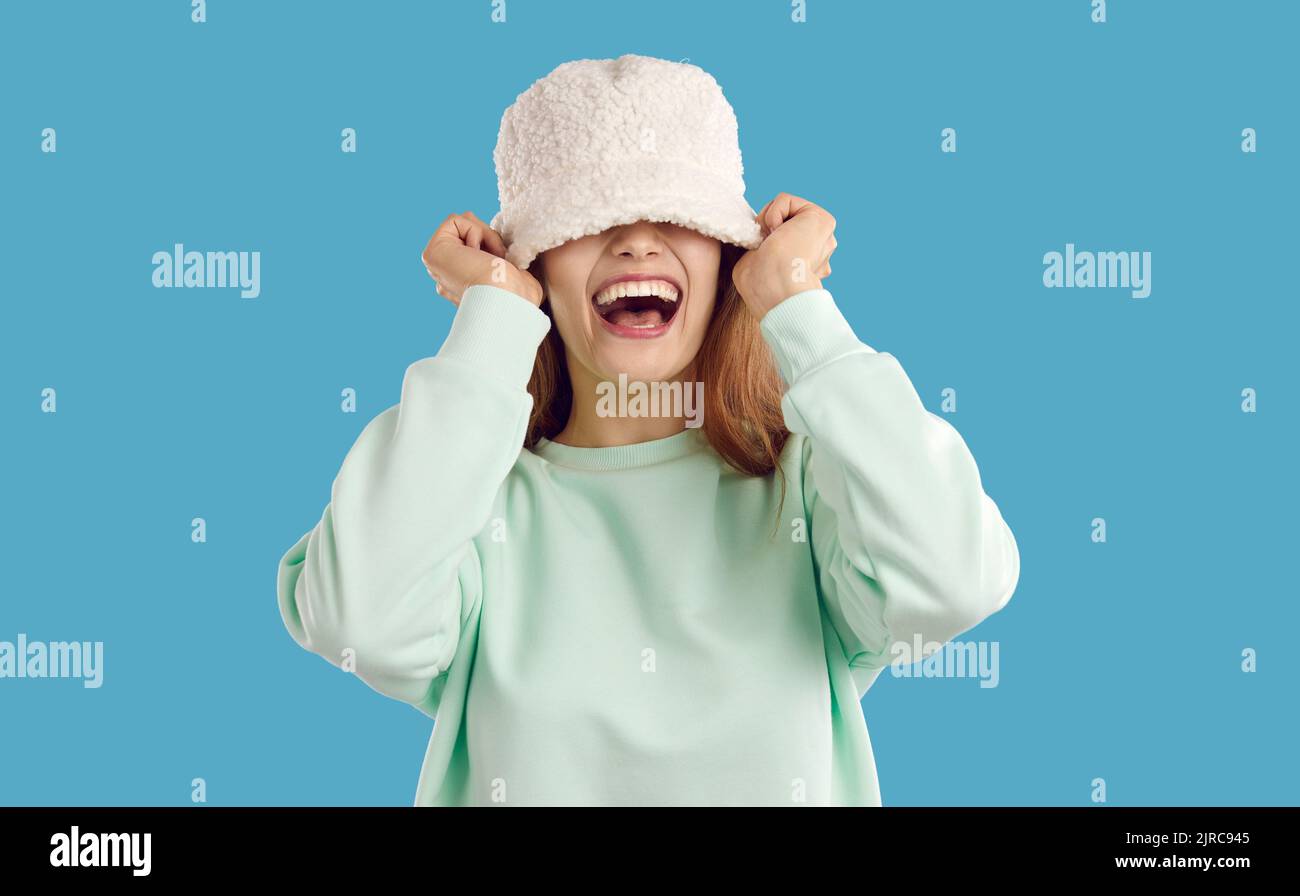 Cheerful funny young woman or teenage girl covers her eyes with faux fur bucket hat Stock Photo