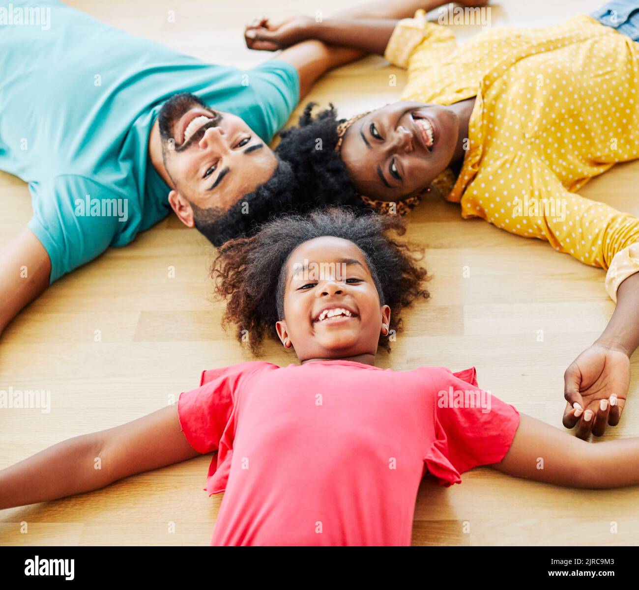 child daughter family happy mother father floor lying down fun together girl cheerful group team teamwork home black Stock Photo