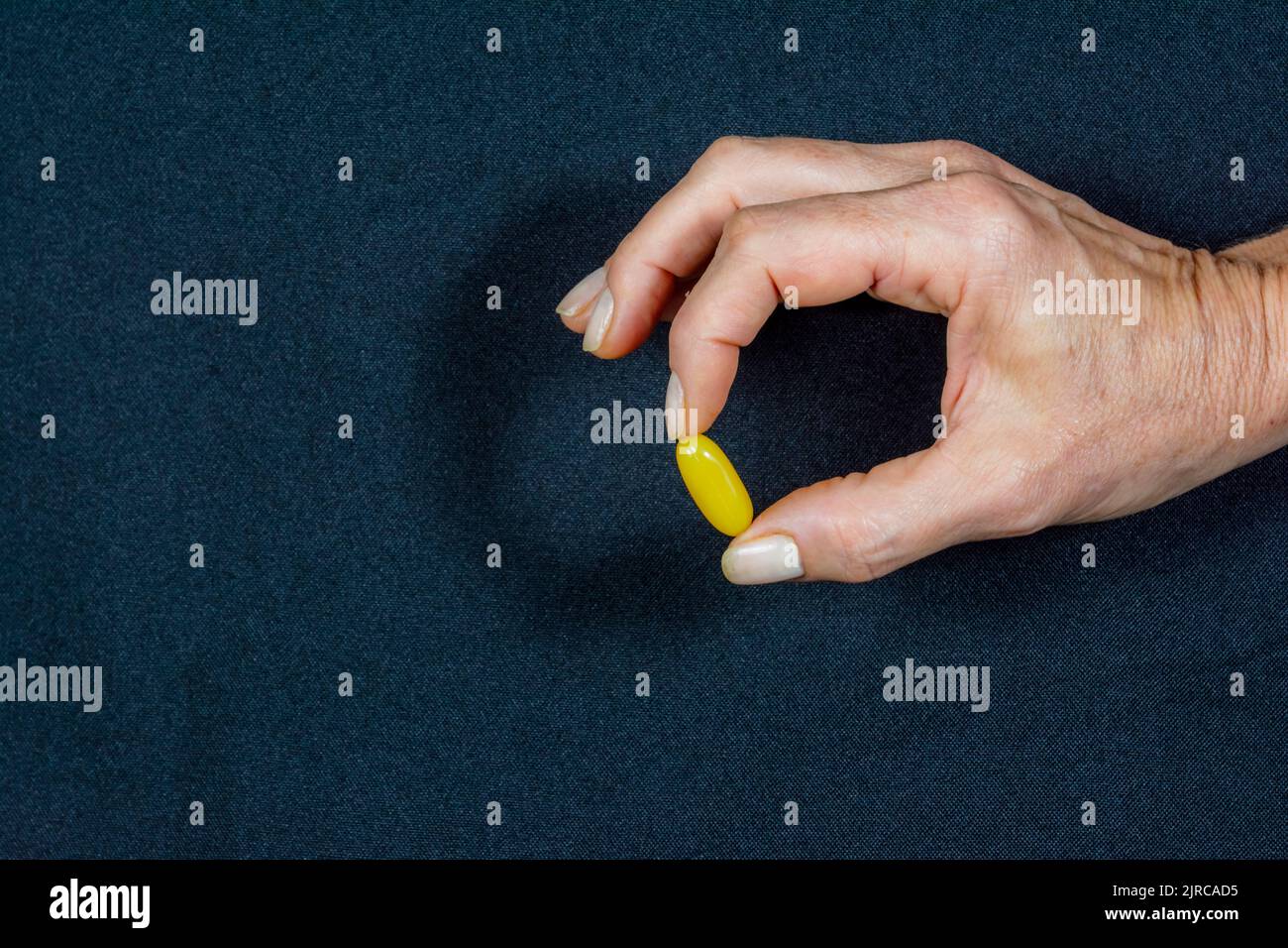 A yellow pill held by the fingers of one hand against a black