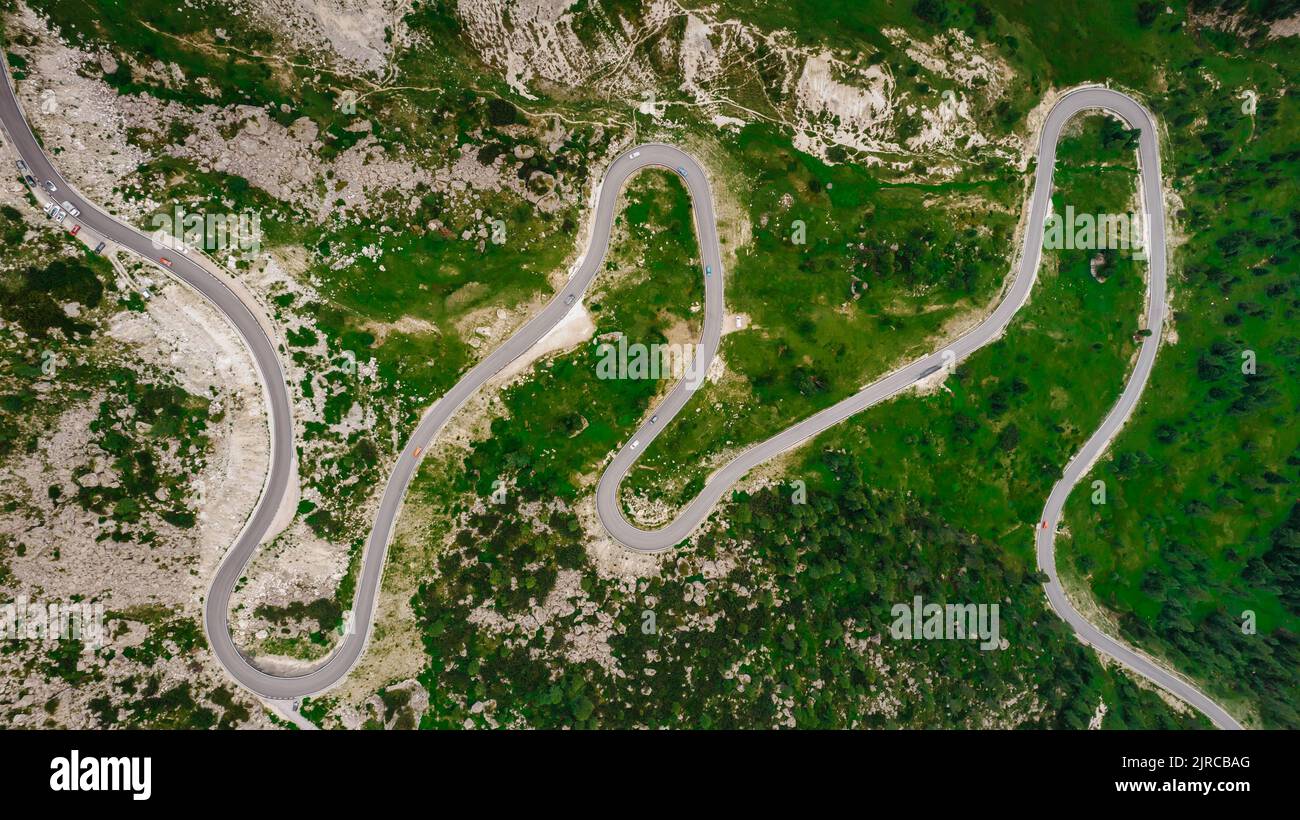 Winding road from high mountain pass in Dolomites, Italy. Great road trip through dense woods and meadows. Aerial view. Curvy road in summer forest sc Stock Photo
