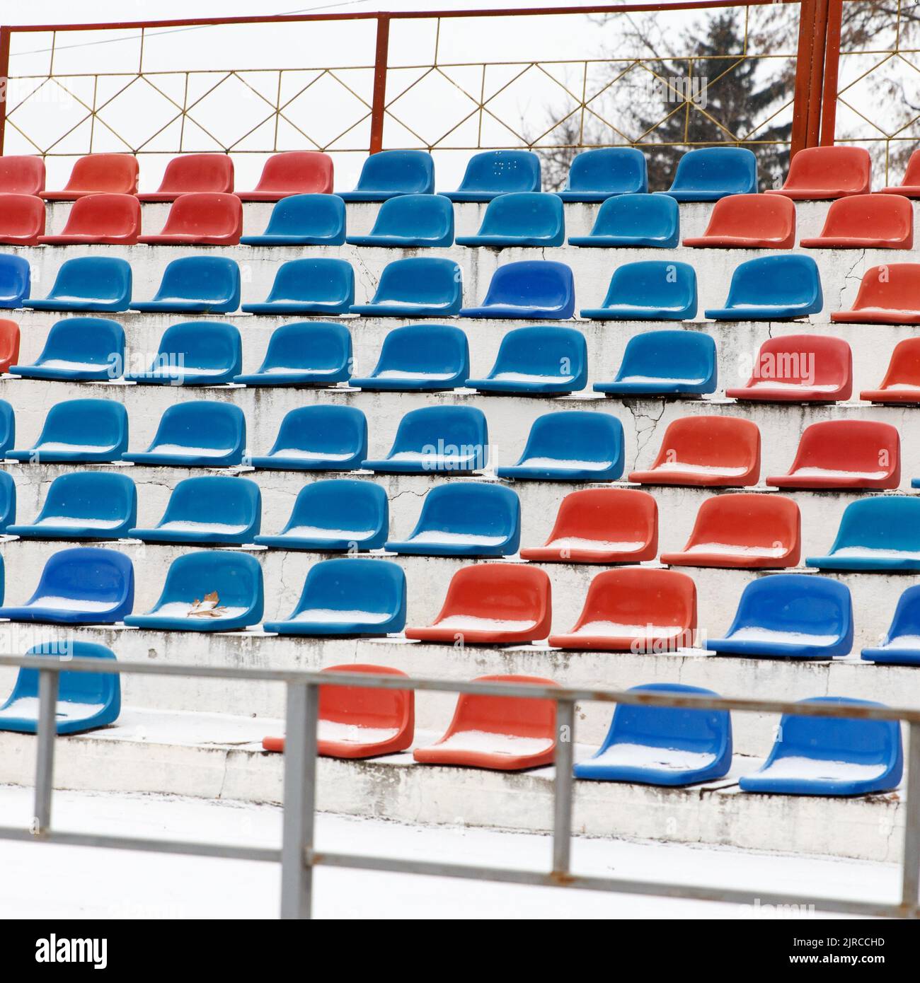 Places where fans sit, plastic red and blue chairs in a football stadium, in winter in snowy weather Stock Photo