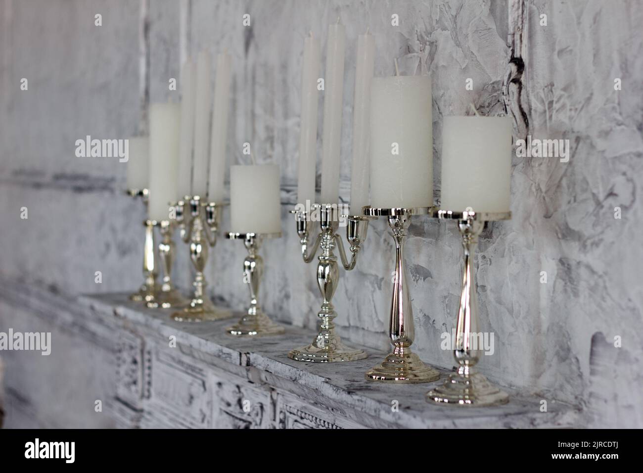 White candles in elegant candlesticks stand on a fireplace in the room Stock Photo