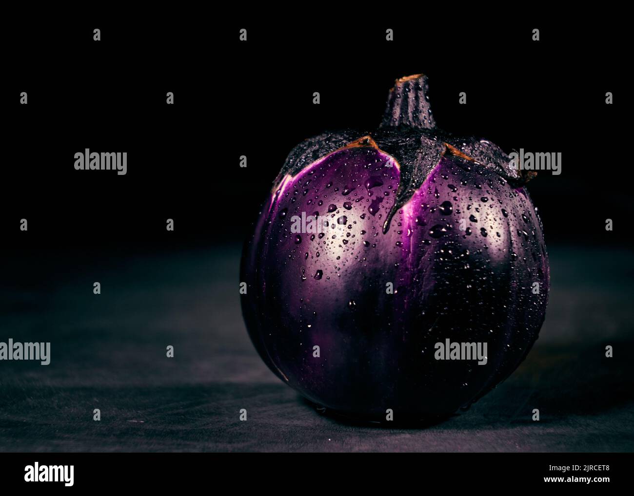 One round eggplant with water drops on a dark background Stock Photo