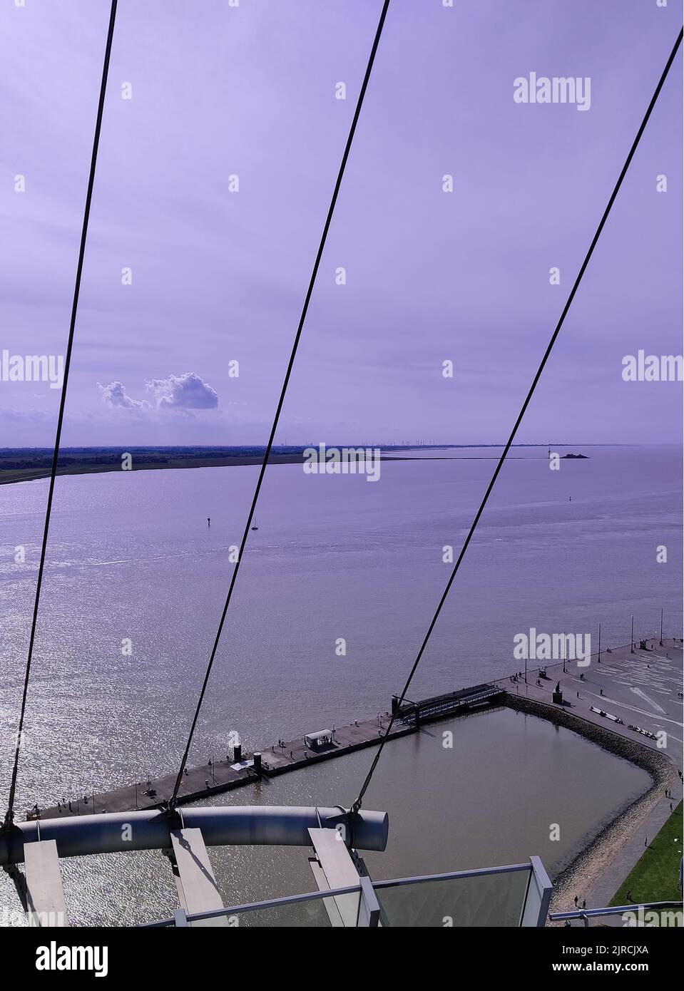 A vertical shot of the ocean from a bridge with suspender cables with the sky illuminating purple Stock Photo