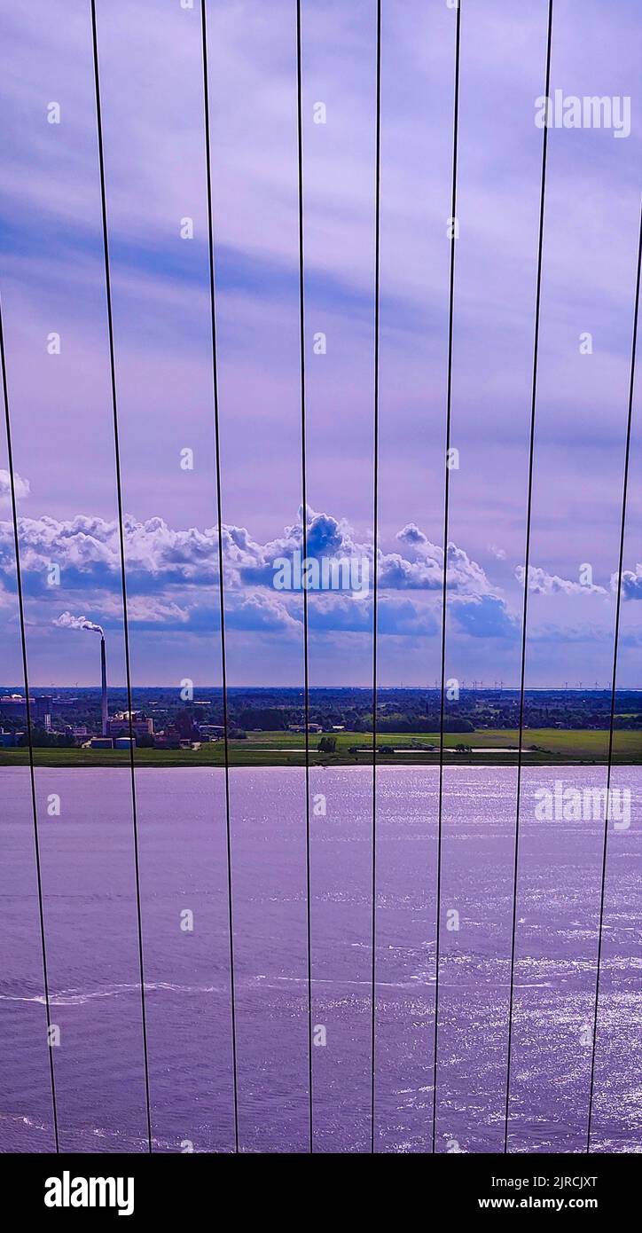 A vertical shot of a coastal city from a bridge with suspender cables with the sky illuminating purple Stock Photo
