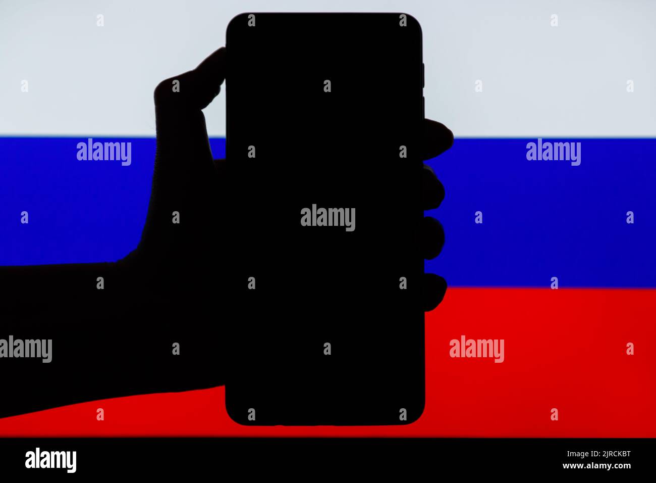 Silhouette of black hand holding mobile with Russian flag in background. Sanctions against Russia concept. Stock Photo