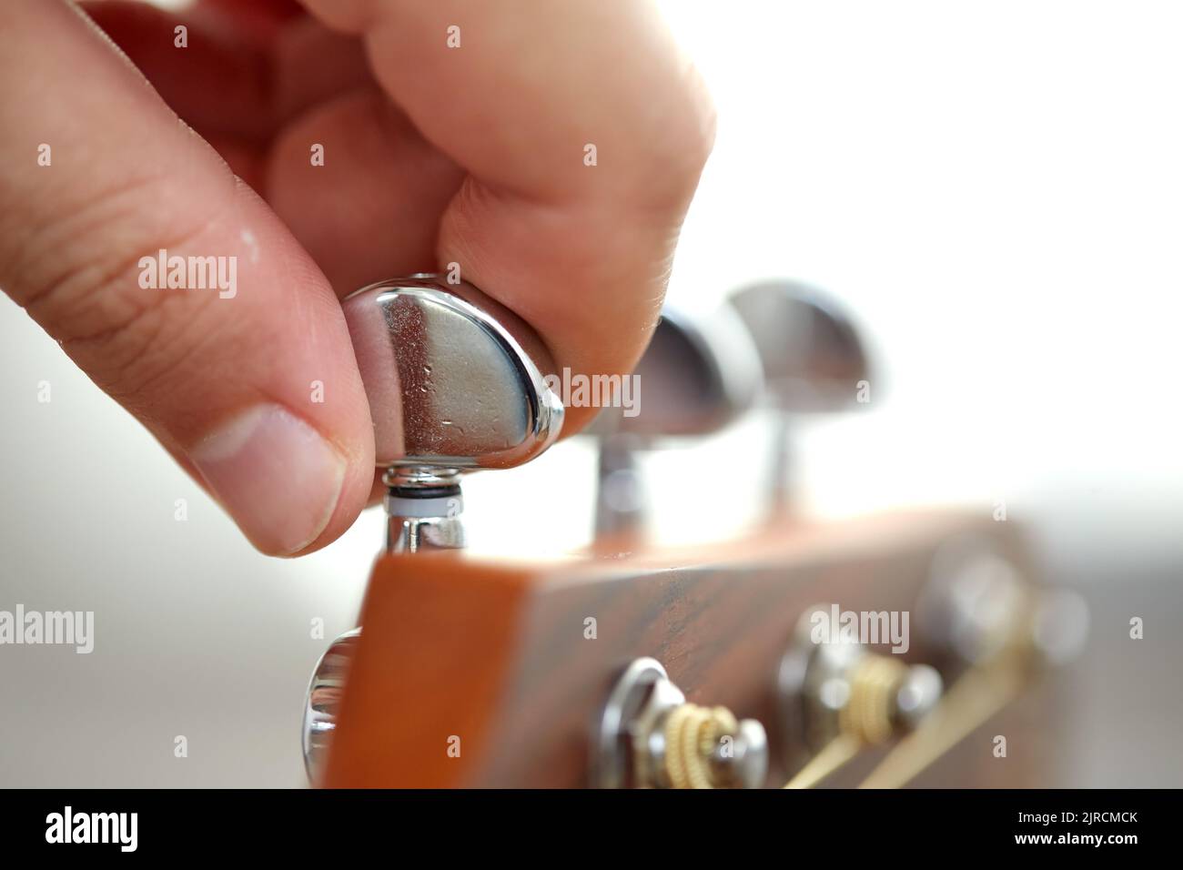 close up of hand tuning guitar strings with pegs Stock Photo