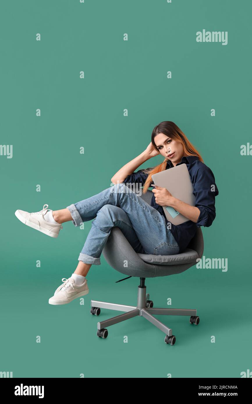 Transgender programmer with laptop sitting on chair against green ...