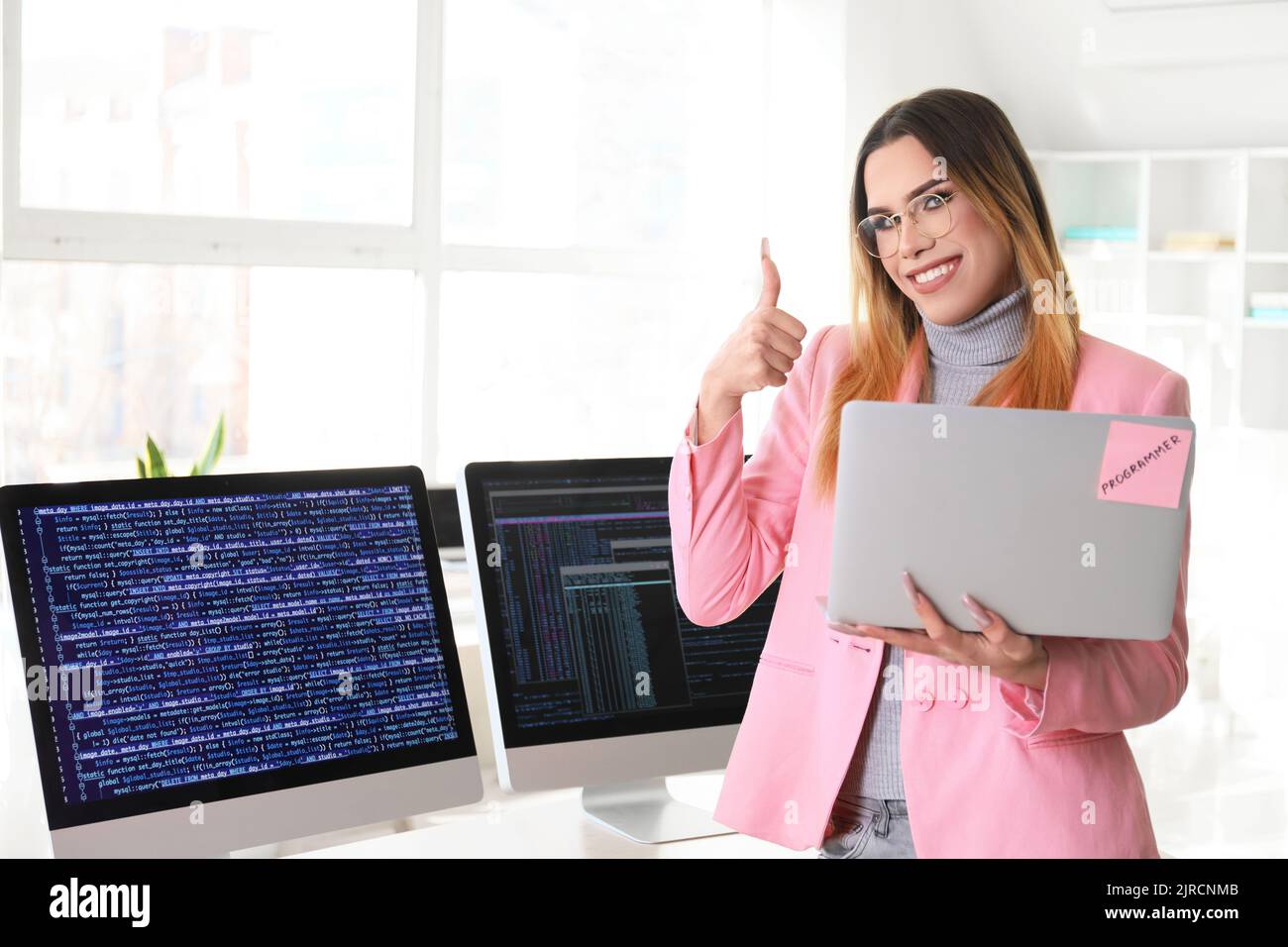 Transgender programmer with laptop showing thumb-up in office Stock ...