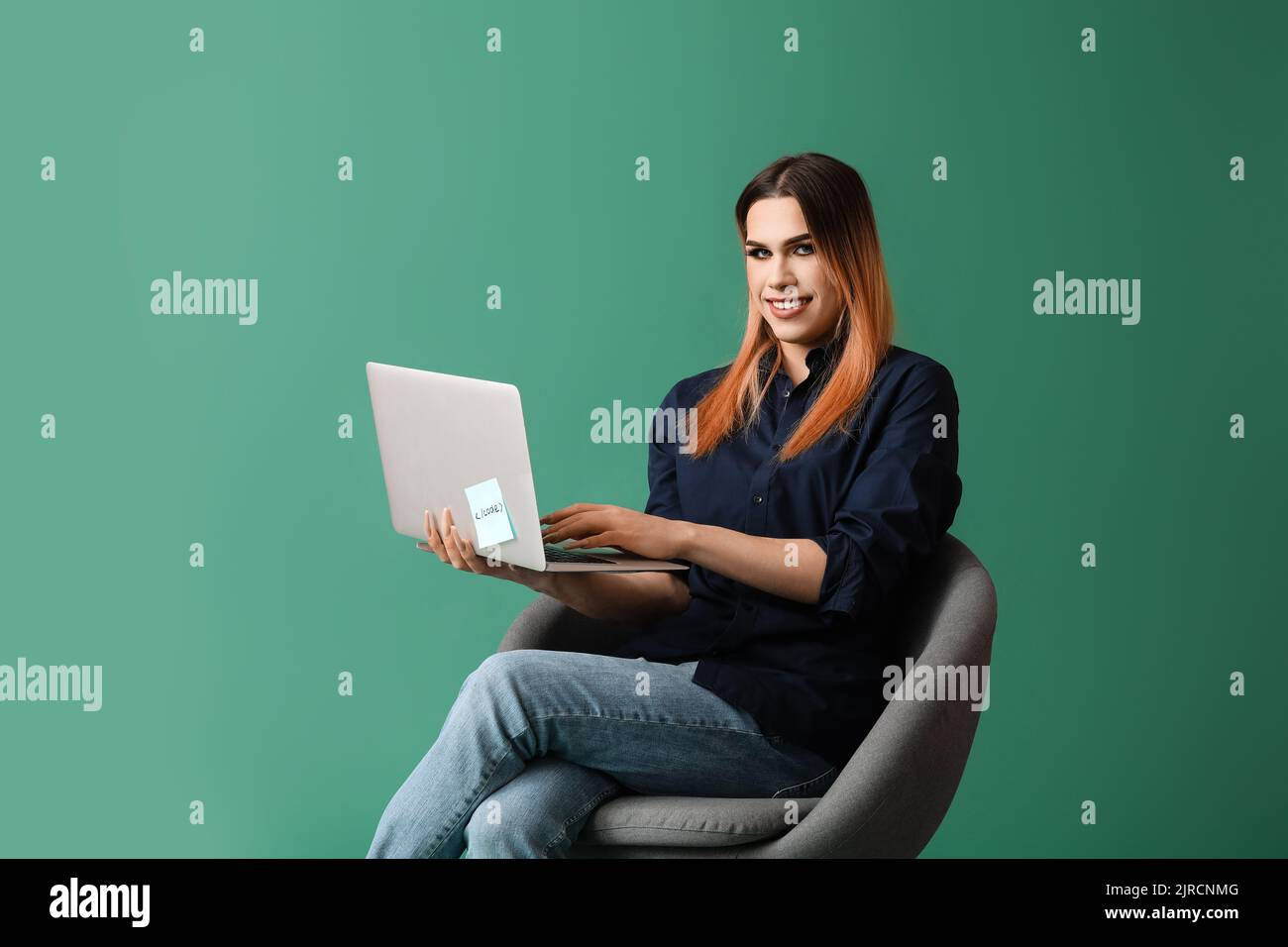 Transgender programmer with laptop sitting on chair against green ...