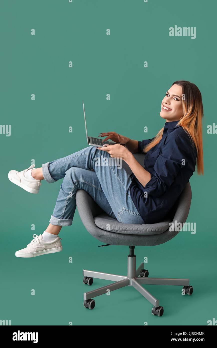 Transgender programmer with laptop sitting on chair against green ...