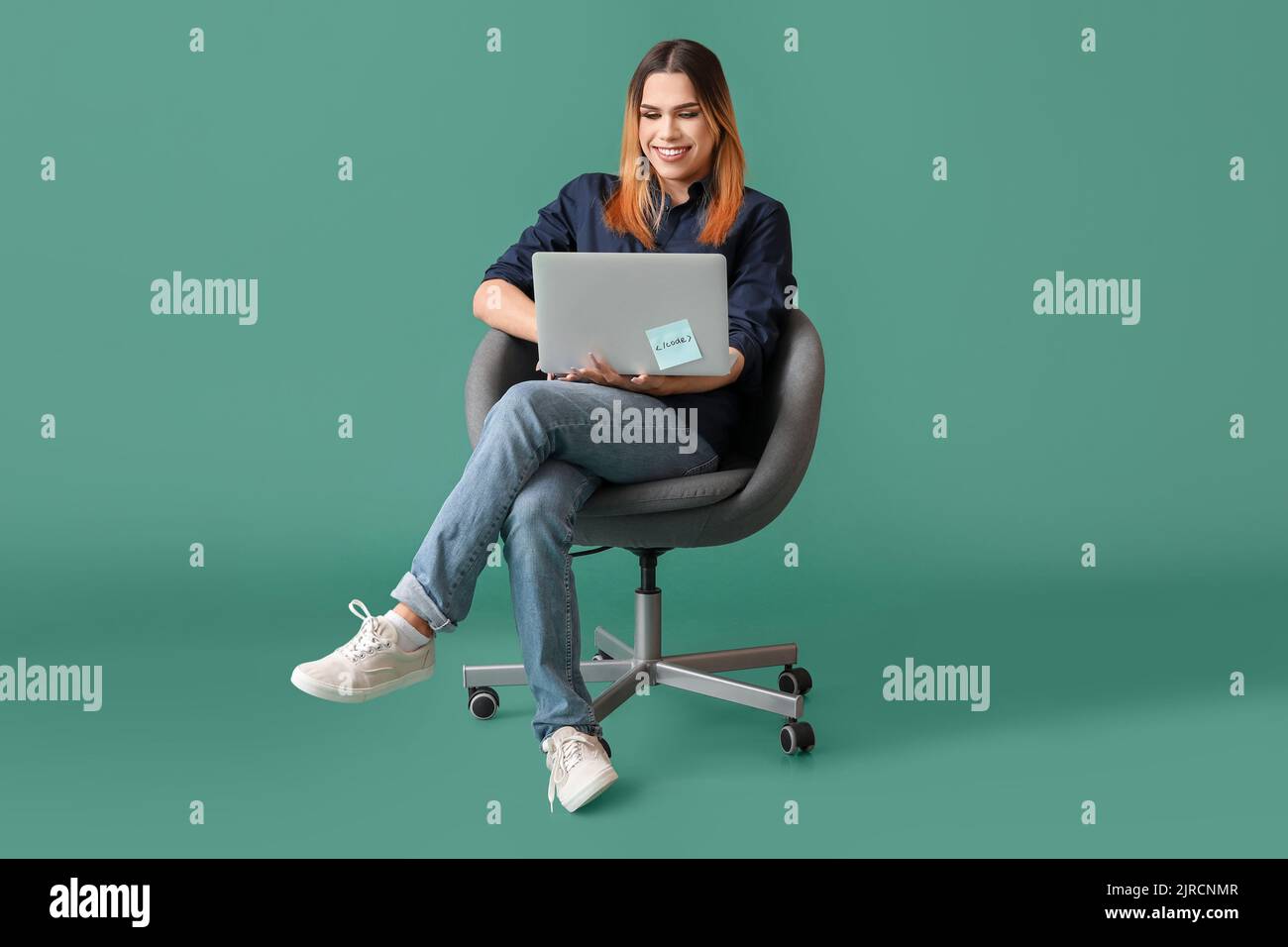 Transgender programmer with laptop sitting on chair against green ...