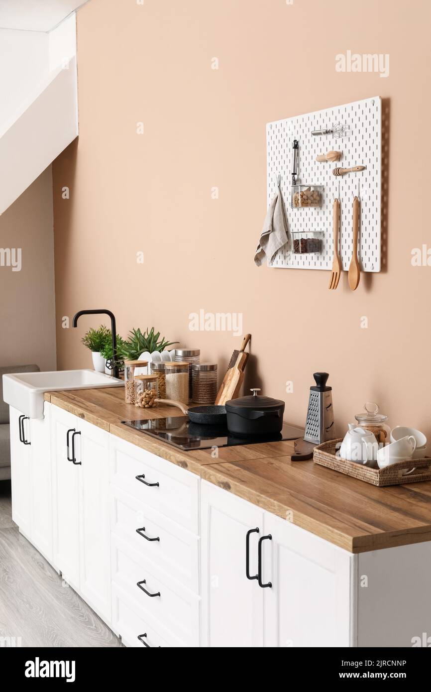 Interior of stylish kitchen with white counters, utensils and pegboard ...