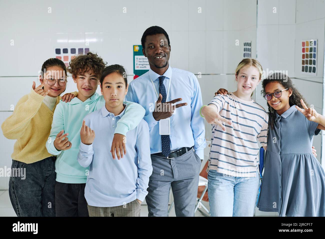 Portrait of smiling teacher posing with diverse group of children and ...