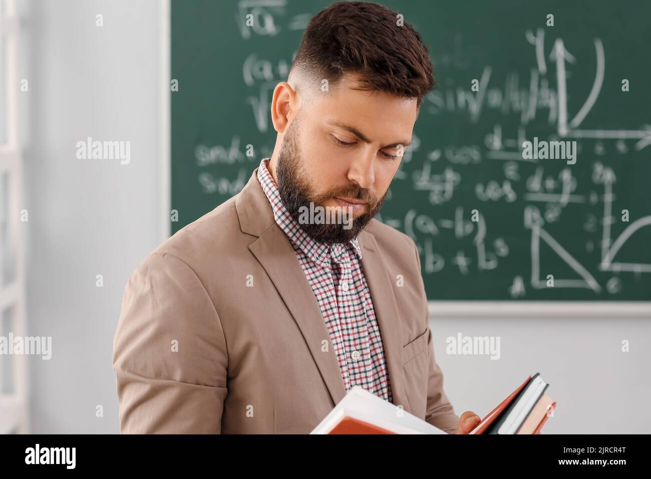 Handsome Math teacher reading book in classroom Stock Photo