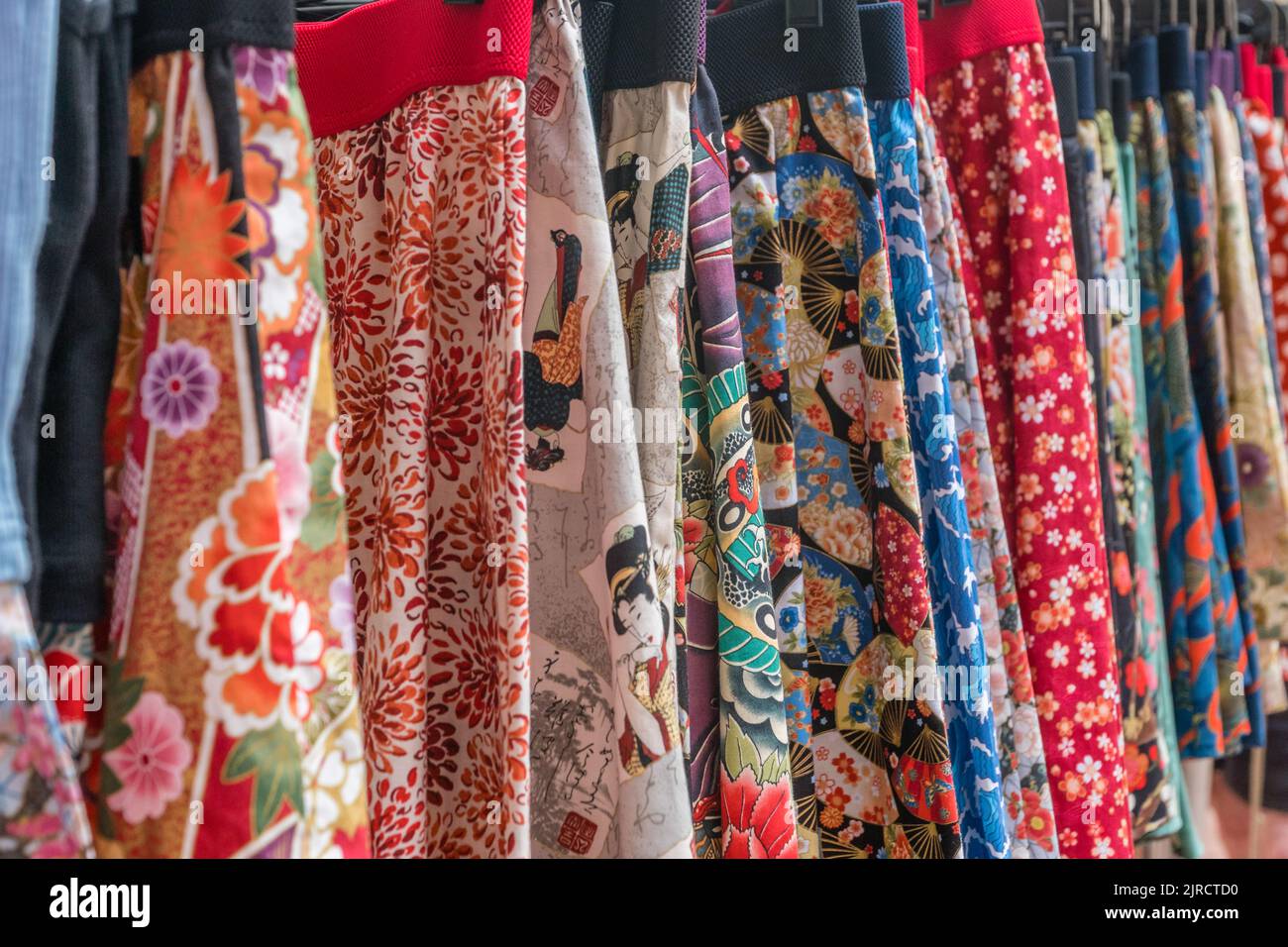 Row of colorful skirts in different fabrics for sale at outdoor market stall. Stock Photo