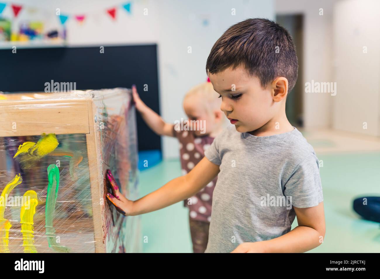 Cling wrap painting for improving kids imagination and brain development. Toddlers finger painting with tempera paints on a cling film wrapped around the wooden shelving stand. Fun activity for kids fine and gross motor skills at the nursery school. High quality photo Stock Photo