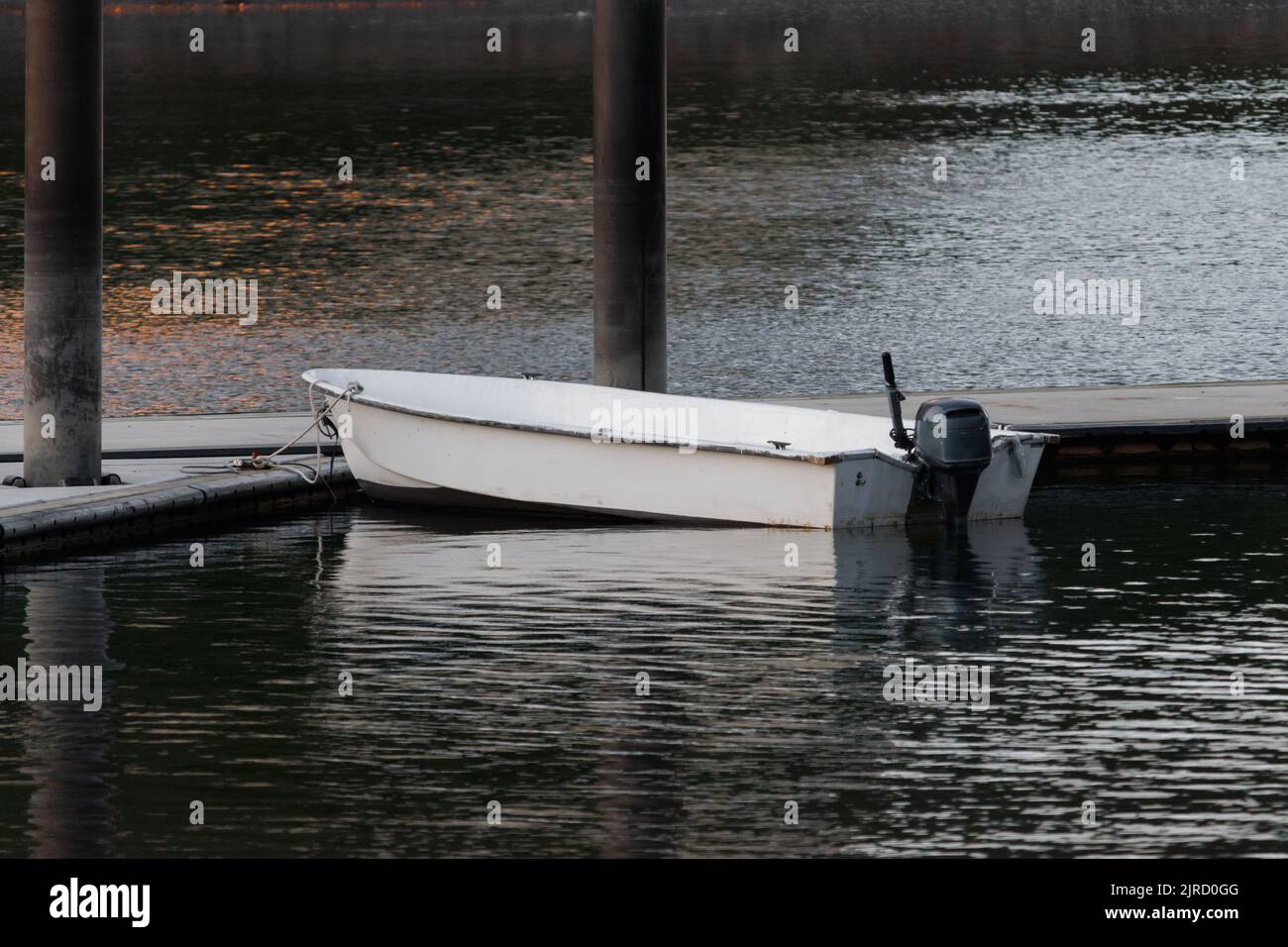 an empty white motorboat tied to a dock in rippling water on a summer evening Stock Photo