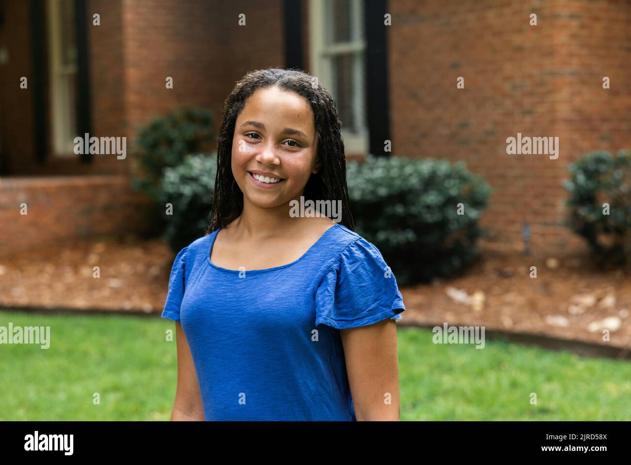 Middle School aged girls in a blue dress standing outside her home for a portrait Stock Photo