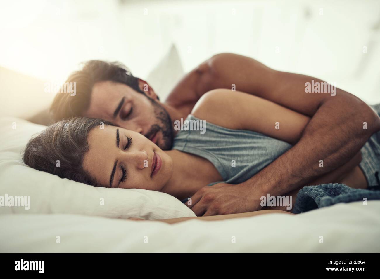 Finding comfort in his arms. an affectionate young couple sleeping in their bed. Stock Photo
