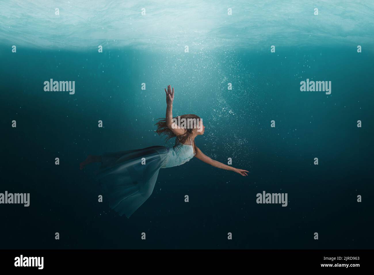 Girl floating in a surreal, dreamlike state under the deep waters of the ocean. Stock Photo