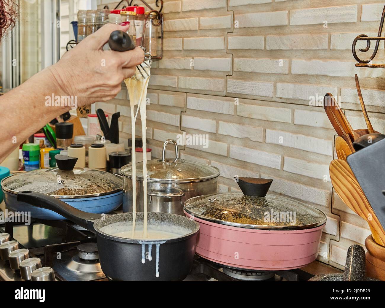 Chef stirs the bechamel sauce, which is cooked on gas stove, into ...