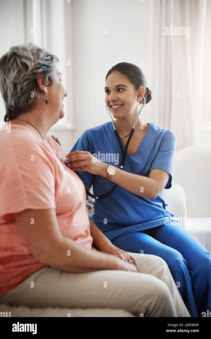 All seems to be sounding quite healthy. an attractive young female nurse examining a senior patient with a stethoscope. Stock Photo