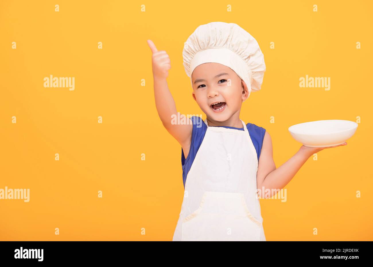 Happy boy in chef uniform showing thumbs up on yellow background Stock Photo
