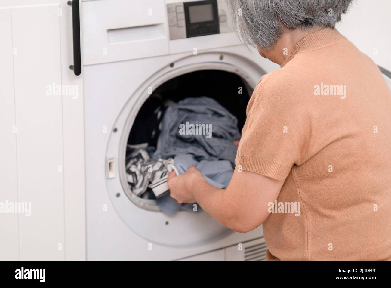Contented senior housewife doing laundry in the laundry room with