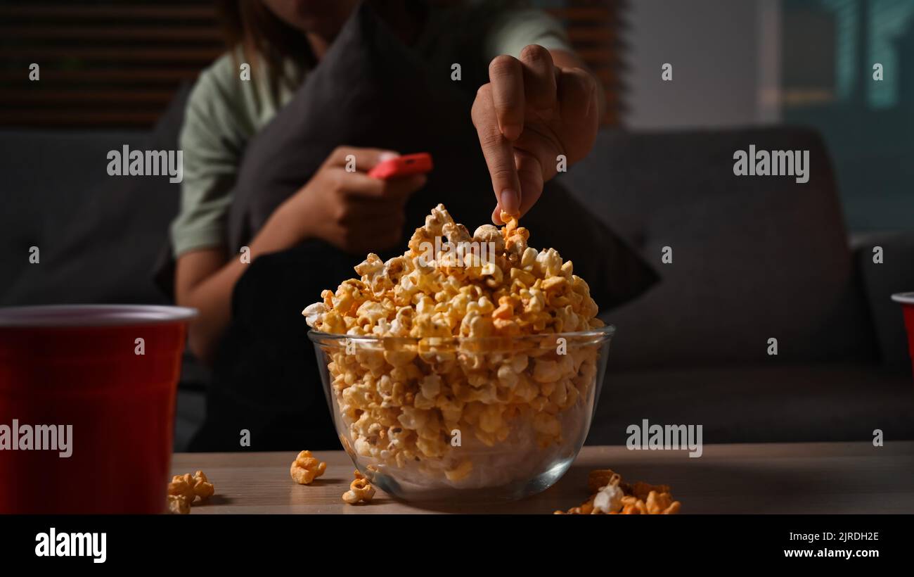 Young lady with remote control eating popcorn and watching movie at