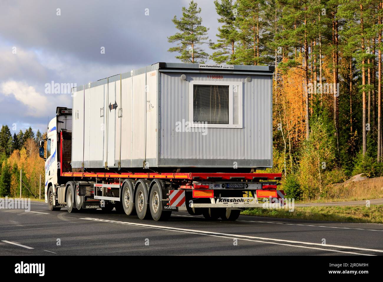 Truck hauls portable cabin on flatbed trailer along highway 2 on a sunny day of autumn, rear view. Lohja, Finland. October 16, 2020. Stock Photo