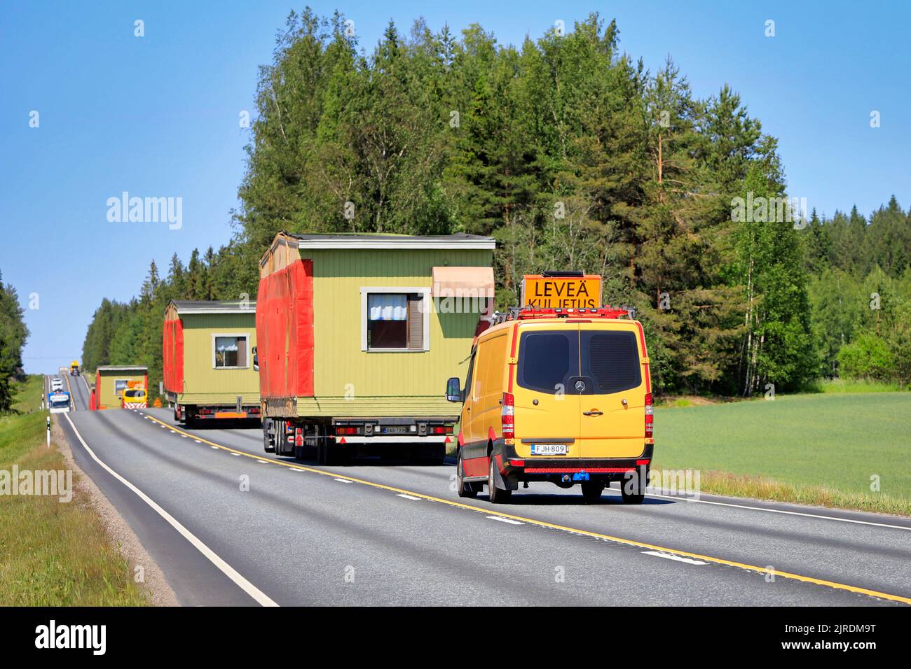 Convoy of trucks hauling portable cabins as oversize loads accompanied by escort vehicles on road, rear view. Jokioinen, Finland. June 15, 2020. Stock Photo