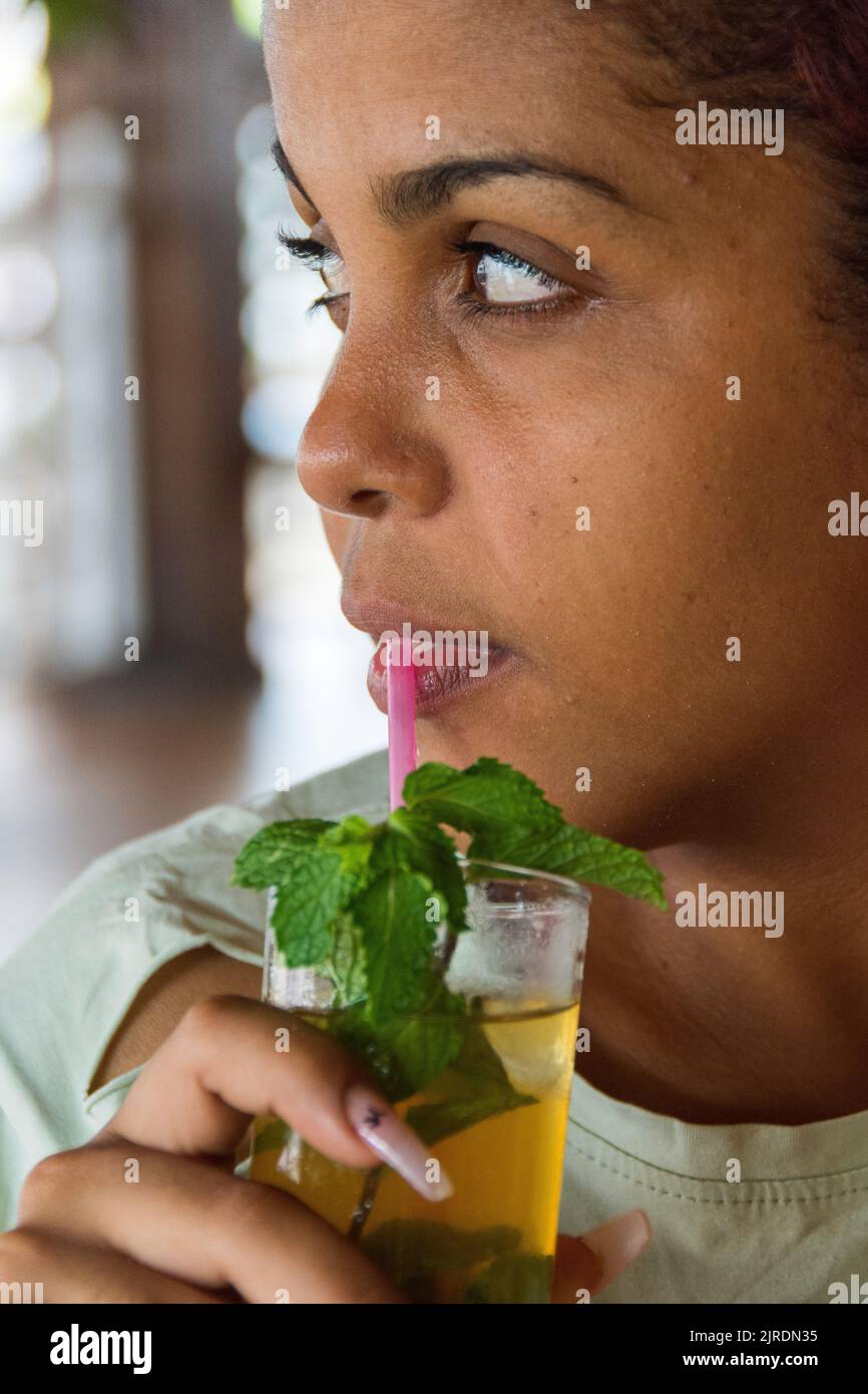 A 22 year old Cuban, female sipping her Mojito cocktail, Varadero Beach, Cuba. Stock Photo