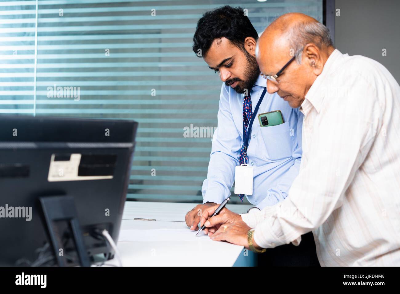 Focus on banker, Employee helping or guiding old man to fill receipt or to fill banking documents at desk - concept of client agreement, elderly Stock Photo