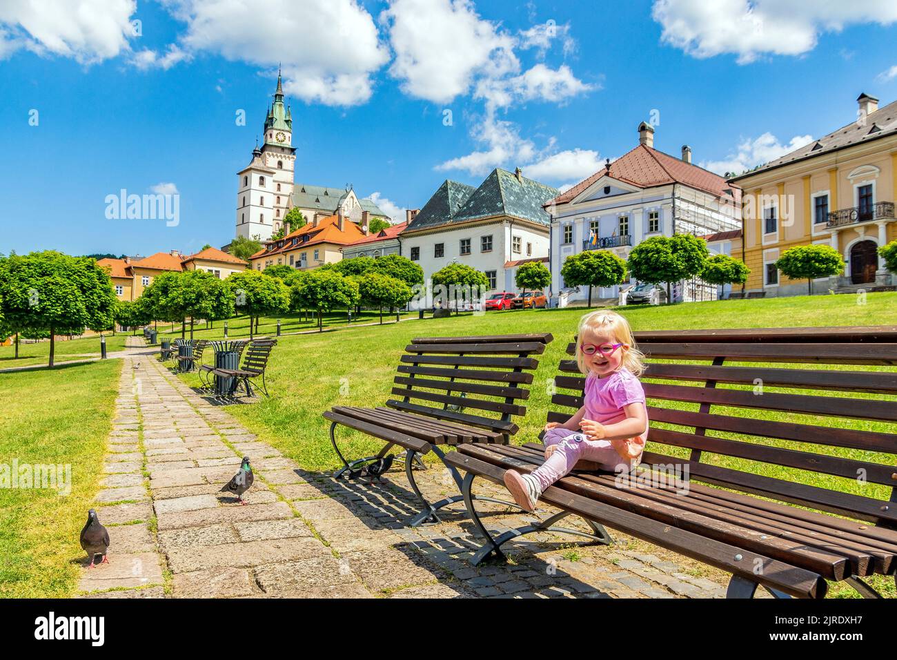 A cute Caucasian girl sitting on a bench in golden town Kremnica Stock ...