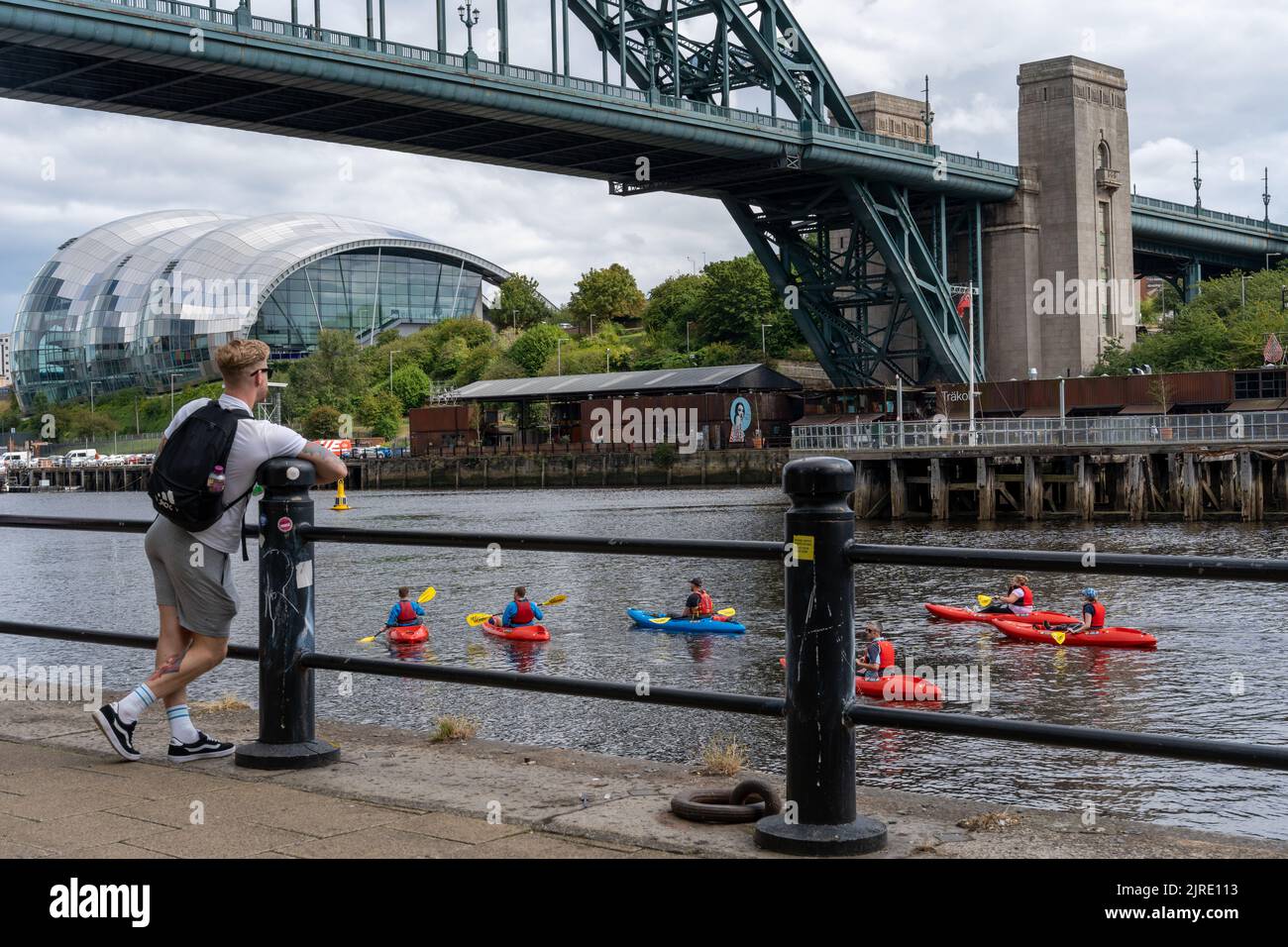 A man stands watching a kayaking lesson on the River Tyne, under the