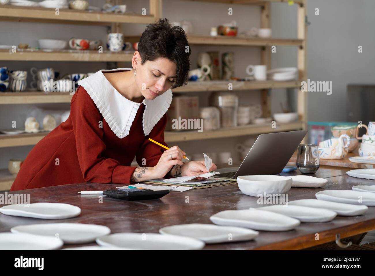 Pensive focused female master potter calculating material costs in her